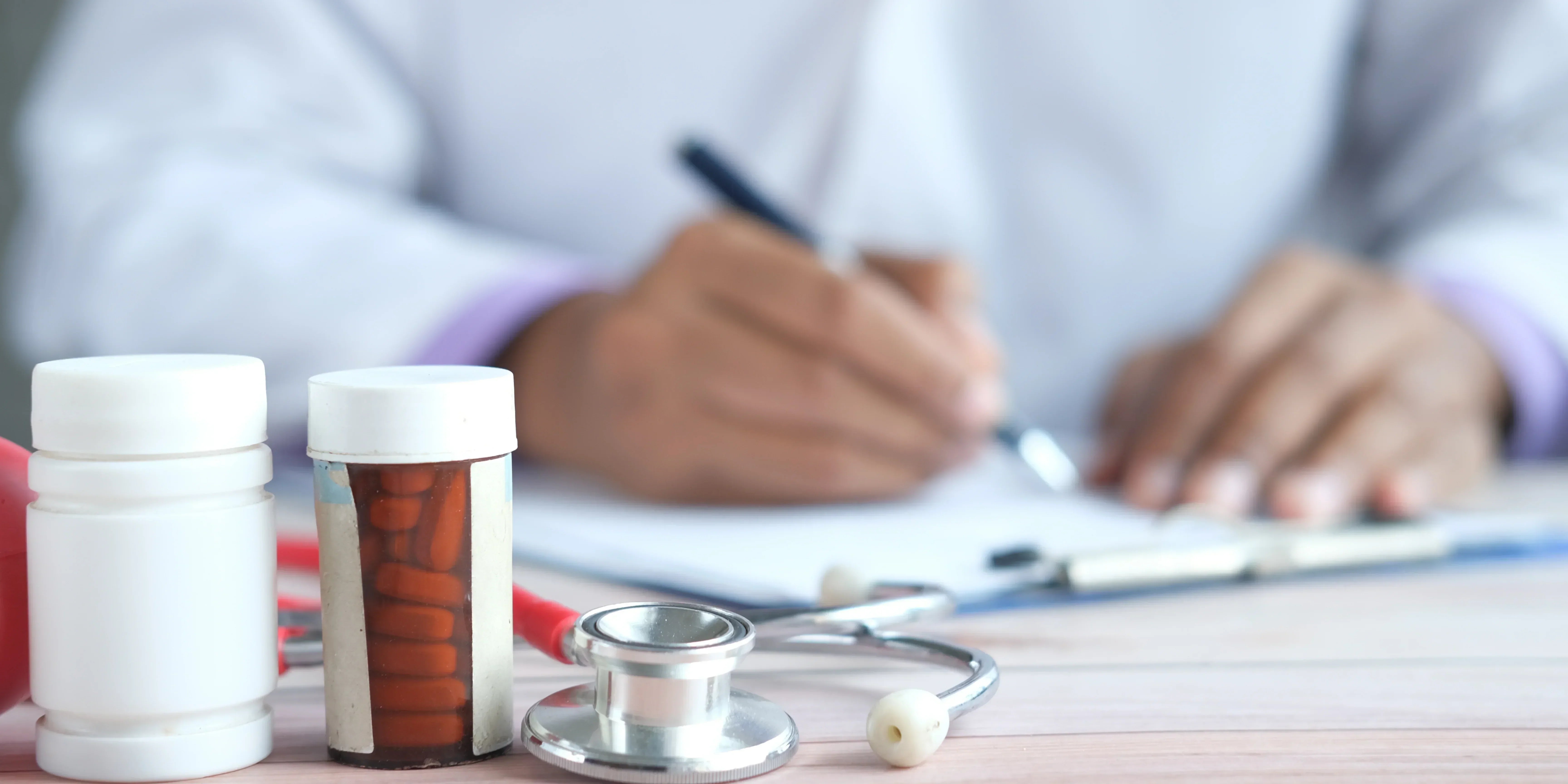 Close up van een dokter die aan het schrijven is over de supplimenten van Tyranos tegen gewrichtspijn en Artrose met twee potjes medicatie voor zijn hand.